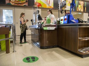 Separated by a plexiglass shield, Samantha McCarter purchases sushi and ice tea from Andrea Nordemann-Dasilva at the Sobeys Extra store in London, Ont. on Wednesday May 27, 2020.