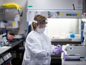 Katie Kempton, a laboratory technologist at LifeLabs, wears protective equipment including a face mask and face shield as she puts on a second pair of gloves before demonstrating how a specimen is tested for COVID-19 at the company's lab, in Surrey, B.C., on Thursday, March 26, 2020.