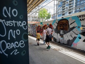 People walk past a mural of George Floyd in Graffiti Alley in Toronto on June 11, 2020. The well known Toronto alleyway is being painted with prominent black figures and messages of solidarity against anti-black racism in support of the Black Lives Matter movement.