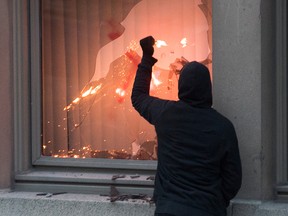 A protester puts a flare through a window during a demonstration calling for justice in the death of George Floyd and victims of police brutality in Montreal, Sunday, May 31, 2020.