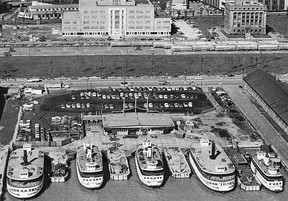 In this c1953 aerial photo of the Toronto City Ferry Docks, we see five of the vessels in the Toronto Island fleet operated by the Toronto Transportation Commission (name changed to Toronto Transit Commission coincident with the addition of the Yonge rapid transit service the following year). At the time of this photo, the Docks were located on the south side of Queen's Quay between Bay and York Sts. From left to right, the photo caption identifies the ferries as Bluebell (steam and scrapped), Sam McBride, Thomas Rennie, (both diesel), Trillium (steam and restored) and William Inglis (diesel). The two steam-powered ferries are just a few years away from retirement. An interesting sidelight to this photograph is the presence at the very top of the image of the TTC's Harbour Yard. It was here, starting in September 1951, that a number of the Peter Witt motors and trailers were stored while a portion of the Eglinton Car Yard, where they were usually stored when not in service, was closed as work progressed on the Eglinton Terminal of the new Yonge subway. Behind the stored streetcars is the long demolished Workmens' Compensation Building built in 1953 to be repurposed as the OPP's provincial headquarters in 1975. To the extreme right is the still stately Toronto Harbour Commission Building, now almost lost in a sea of office towers and condominiums.