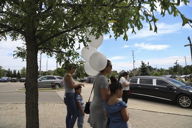 A woman holding four symbolic white balloons stands with her children outside St. Eugene De Mazenod Catholic Church in Brampton as the funeral for  Karolina Ciasullo and their three daughters Klara, Mila and Lilianna - who were killed last Thursday - arrive at the church for the funeral service  . Jack Boland/Toronto Sun/Postmedia Network