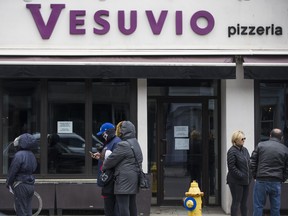 A masked customer waits for their order outside of Vesuvio in The Junction neighbourhood in Toronto, Ont. on Wednesday, April 15, 2020.  The long-running Italian restaurant closed in the midst of the COVID-19 pandemic.