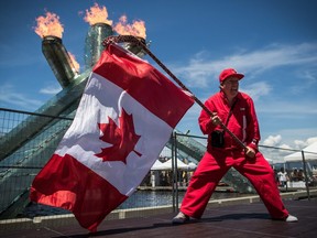 Ricky Johnson waves a Canadian flag on a hockey stick as the Olympic cauldron burns while attending Canada Day celebrations in Vancouver, on Monday July 1, 2019.