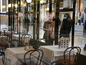 A woman wearing a respiratory mask stands in front of a restaurant doorway.