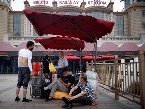 People sit on their luggage outside the Beijing Railway Station, after an outbreak of the coronavirus disease (COVID-19), in Beijing, China July 3, 2020.