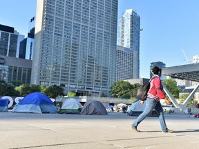 A pedestrian walks by the tent city occupying much of Nathan Phillips Square in front of Toronto City Hall on Tuesday, July 7 2020.