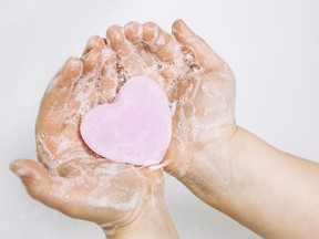Importance of personal hygiene care. Flat lay view of child washing dirty hands with pink heart shape soap bar, lot of foam. Copy space.