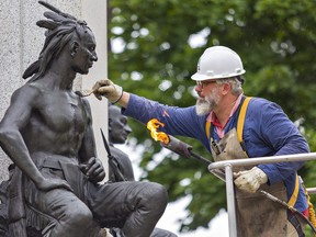 Alexander Gabov, an art conservator, applies hot wax to a statue at the Joseph Brant monument on June 22, 2020 in downtown Brantford.