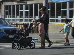 Two women and their young children walk by the corner of Seaton St. And Dundas St. East viewing the aftermath of where a man in his late 20s was found by Toronto Police on Sunday July 26, 2020.
