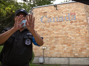 A security officer wearing a face mask to help protect against the coronavirus gestures outside the Canadian Embassy in Beijing, Thursday, Aug. 6, 2020.