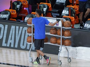 A worker wheels away the warmup basketballs from the Milwaukee Bucks bench after the scheduled start of their game on Wednesday was postponed following the teams boycott.