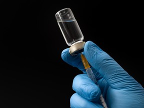 Insulin shot, flu jab or medical injection concept theme with doctor or nurse hands wearing blue surgical latex gloves filling a syringe from a glass vial isolated on black background with copy space