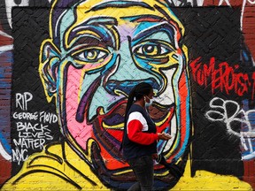 A woman walks by a mural of George Floyd, in the aftermath of his death in Minneapolis police custody, on the lower east side of New York City, Aug. 7, 2020.
