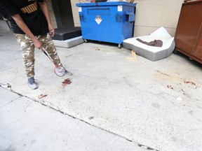 Street person Dee walks uses a badminton racket to point to a blood stain in O'Keefe Lane, near Yonge-Dundas Square, on Saturday, Aug. 29, 2020, the morning after a man, 20, was stabbed in the laneway.
