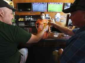 David Reay (L) and Casey Kemp enjoy some beers with bartender Tonya MacWilliams (middle) at the Fill Station Sports Bar in the Beach on Queen St. East. Bars and restaurants opened in Toronto as part of Phase 3 of COVID rules. People were enjoying socializing, social distancing watching sports at the  on Saturday August 1, 2020.