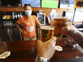 A couple of bar patrons enjoy some beers with bartender Tonya MacWilliams at the Fill Station Sports Bar in Toronto, Aug. 1, 2020.