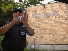 A security officer wearing a face mask to help protect against the coronavirus gestures outside the Canadian Embassy in Beijing, Thursday, Aug. 6, 2020.