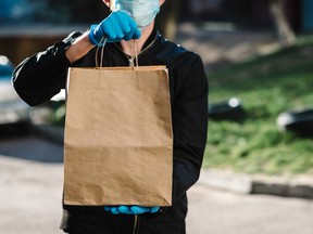 Courier in protective mask, medical gloves delivers takeaway food.  Employee hold cardboard package. Place for text. Delivery service under quarantine, 2019-ncov, pandemic coronavirus, covid-19.