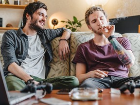 Young hipster guy smoking marijuana joint while relaxing with friend at home.