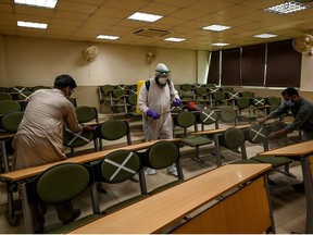 A worker wearing a Personal Protective Equipment (PPE) suit (C) sprays disinfectant while other workers tag cross signs on chairs for social distancing at the Capital University of Science and Technology in Islamabad on September 10, 2020, following the government's annoucement about reopening educational institutes starting from September 15, nearly six months after the spread of Covid-19 coronavirus pandemic.
