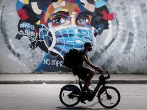 A man wears a face mask as he cycles by a mural defaced by graffiti objecting to mask usage as a measure to protect against the spread of COVID-19, in Montreal, Sunday, Aug 30, 2020.
