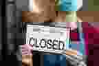 Businesswoman closing her business activity due to covid-19 lockdown. Owner with surgical mask close the doors of her store due to quarantine coronavirus damage. Close up sign of bankrupt business due to the effect of COVID-19 pandemic.