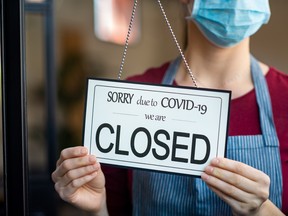 Businesswoman closing her business activity due to covid-19 lockdown. Owner with surgical mask close the doors of her store due to quarantine coronavirus damage. Close up sign of bankrupt business due to the effect of COVID-19 pandemic.