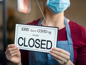 Businesswoman closing her business activity due to covid-19 lockdown. Owner with surgical mask close the doors of her store due to quarantine coronavirus damage. Close up sign of bankrupt business due to the effect of COVID-19 pandemic.