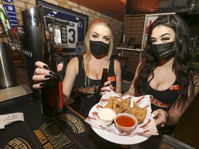 Erin (L) and Ryleigh, staff at the Hooters restaurant at Adelaide and John Sts., serve up beer and wings on Friday, Oct.9, 2020, as the province announces tighter restrictions on Toronto bars and restaurants for 28 days starting Saturday due to surging Covid cases.
