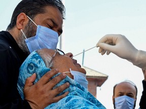 A man holds his mother's head as a medical worker collects a swab sample for a Rapid Antigen Test for COVID-19, in Srinagar, India, Thursday, Oct. 1, 2020.
