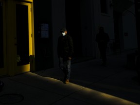 A man wearing a protective mask walks through a shaft of light during the COVID-19 pandemic in downtown Toronto on Thursday, November 12, 2020. THE CANADIAN PRESS/Nathan Denette
