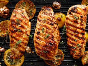 Grilled chicken breasts with thyme, garlic and lemon slices on a grill pan close up, top view.