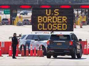 In this file photo, U.S. Customs officers speaks with people in a car beside a sign saying that the U.S. border is closed at the U.S.-Canada border in Lansdowne, Ont., on March 22, 2020.