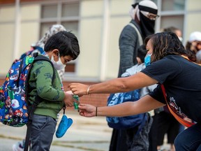 A teacher helps a student close his personal hand sanitizer as he arrives for the first time since the start of the coronavirus disease (COVID-19) pandemic at Hunter's Glen Junior Public School, part of the Toronto District School Board (TDSB) in Scarborough, Ontario, Canada, on September 15, 2020.