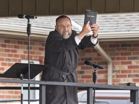 Church of God Pastor Henry Hildebrandt holds up a copy of the Holy Bible for all to see after taking the stage in the church's parking lot in Aylmer, Ontario on Sunday April 26, 2020. (Derek Ruttan/The London Free Press)