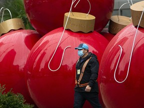 A delivery person wearing a face mask to prevent the spread of COVID-19 walks past giant Christmas tree ornaments in downtown Vancouver on Monday, Dec. 14, 2020.