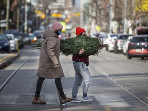 Amy Tsang, joined by Diana Bala, carries a Christmas tree purchased from Sweetpea's along Roncesvalles Ave. in Toronto, Ont.  on Thursday December 3, 2020.
