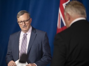 Dr. David Williams, Ontario's Chief Medical Officer, left, and Premier Doug Ford trade places at the podium during a news conference at the Ontario legislature in Toronto on Wednesday, November 25, 2020.