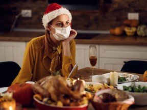 Pensive woman wearing face mask and sitting alone at dining table on Christmas eve.