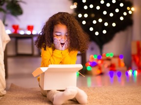 Amazed little afro girl opening Christmas gift near xmas tree