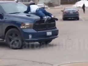 A man clings to the hood of a pickup truck after a heated dispute over a parking job at a shopping plaza in north Toronto on Dec. 10, 2020.