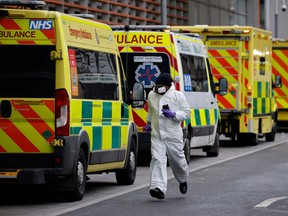 A medical delivery driver wearing PPE runs along a line of parked ambulances outside the Royal London hospital in London on January 19, 2021.
