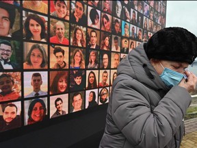 A woman cries in front of a huge screen bearing portraits of late crew members and passengers of Ukraine International Airlines Flight 752, which crashed in Iran a year before, during a commemorative ceremony on Jan. 8, 2021 at the site of a future memorial on the Dnipro river bank in Ukraine's capital Kiev.