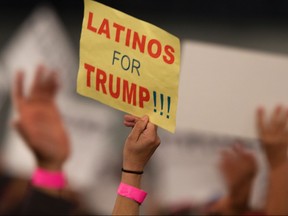 A woman hoods a sign expressing Latino support for former president Donald Trump.