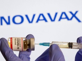 A woman holds a small bottle labelled with a "Coronavirus COVID-19 Vaccine" sticker and a medical syringe in front of a displayed Novavax logo in this photo illustration taken Oct. 30, 2020.