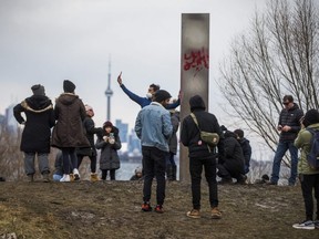 People gather around a steel monolith at Humber Bay Park East in Toronto, Ont. on Friday January 1, 2021. Installed New Years Eve, the mysterious obelisk was discovered defaced by graffiti on New Year's Day.