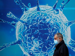 A man wearing a protective face mask walks past an illustration of a virus outside a regional science centre in Oldham, Britain August 3, 2020.