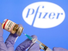A woman holds a small bottle labeled with a "Coronavirus COVID-19 Vaccine" sticker and a medical syringe in front of the displayed Pfizer logo in this illustration taken, October 30, 2020.