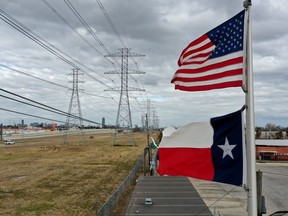 The U.S. and Texas flags fly in front of high voltage transmission towers on February 21, 2021 in Houston, Texas.